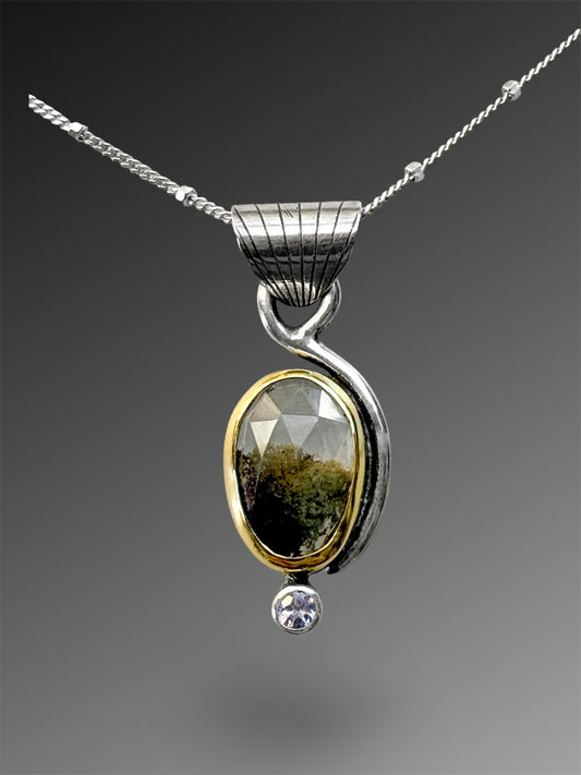 Silver pendant with green gemstone with mossy landscape inclusions and small tanzanite on a gray background